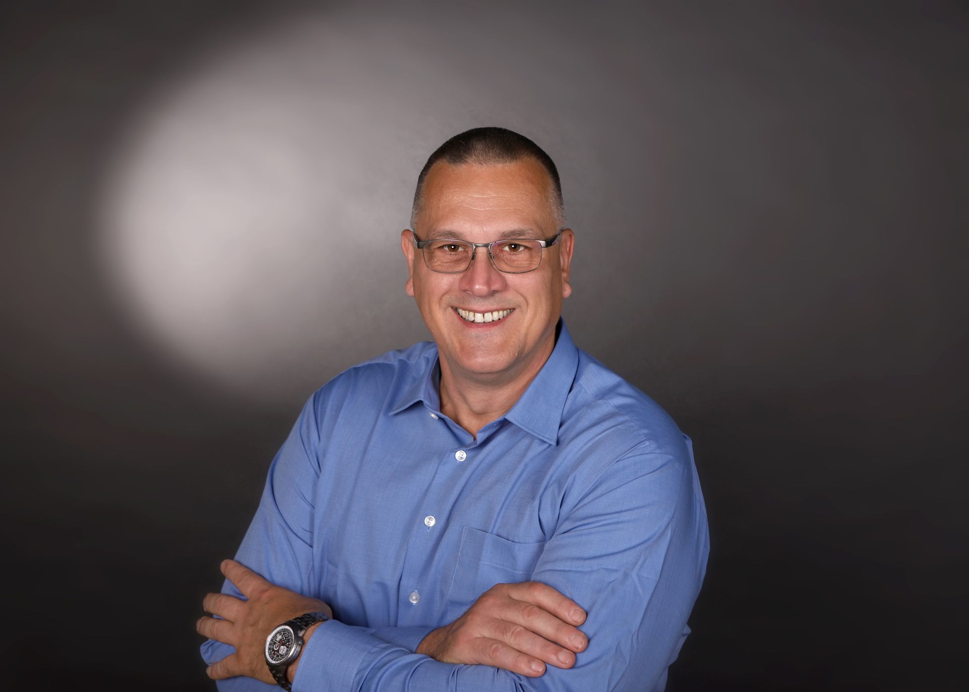 Porträt eines Mannes mit Brille und blauem Hemd, der lächelnd in die Kamera blickt.